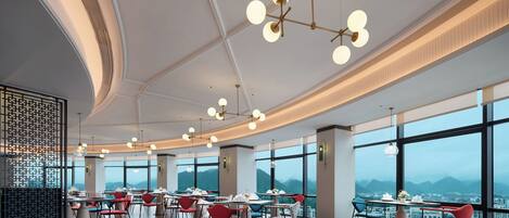 A modern dining area with multiple tables and chairs, large windows offering a mountain view, and contemporary lighting fixtures.