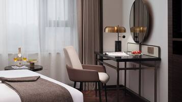 Habitación de hotel con cama, escritorio con lámpara, silla y una pequeña mesa con una botella y vasos.