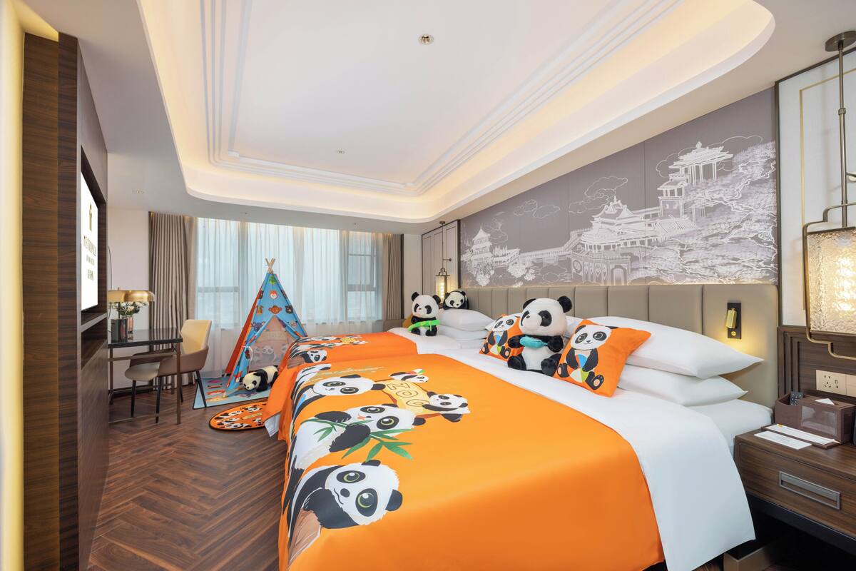 Ein Hotelzimmer mit einem großen Bett, einem Schreibtisch, einem Stuhl und einer Bettdecke mit Panda-Motiv.