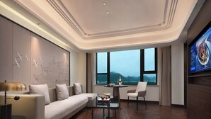 Una habitación de hotel moderna con sofá, mesa de centro, televisor y un ventanal con vistas a las montañas.