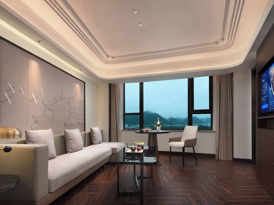 Ein modernes Hotelzimmer mit einer Couch, einem Couchtisch, einem Fernseher und einem großen Fenster mit Bergblick.