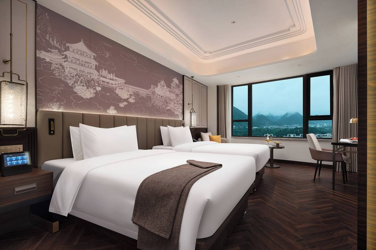 Ein Hotelzimmer mit zwei Betten, einem Schreibtisch und Blick auf Berge.
