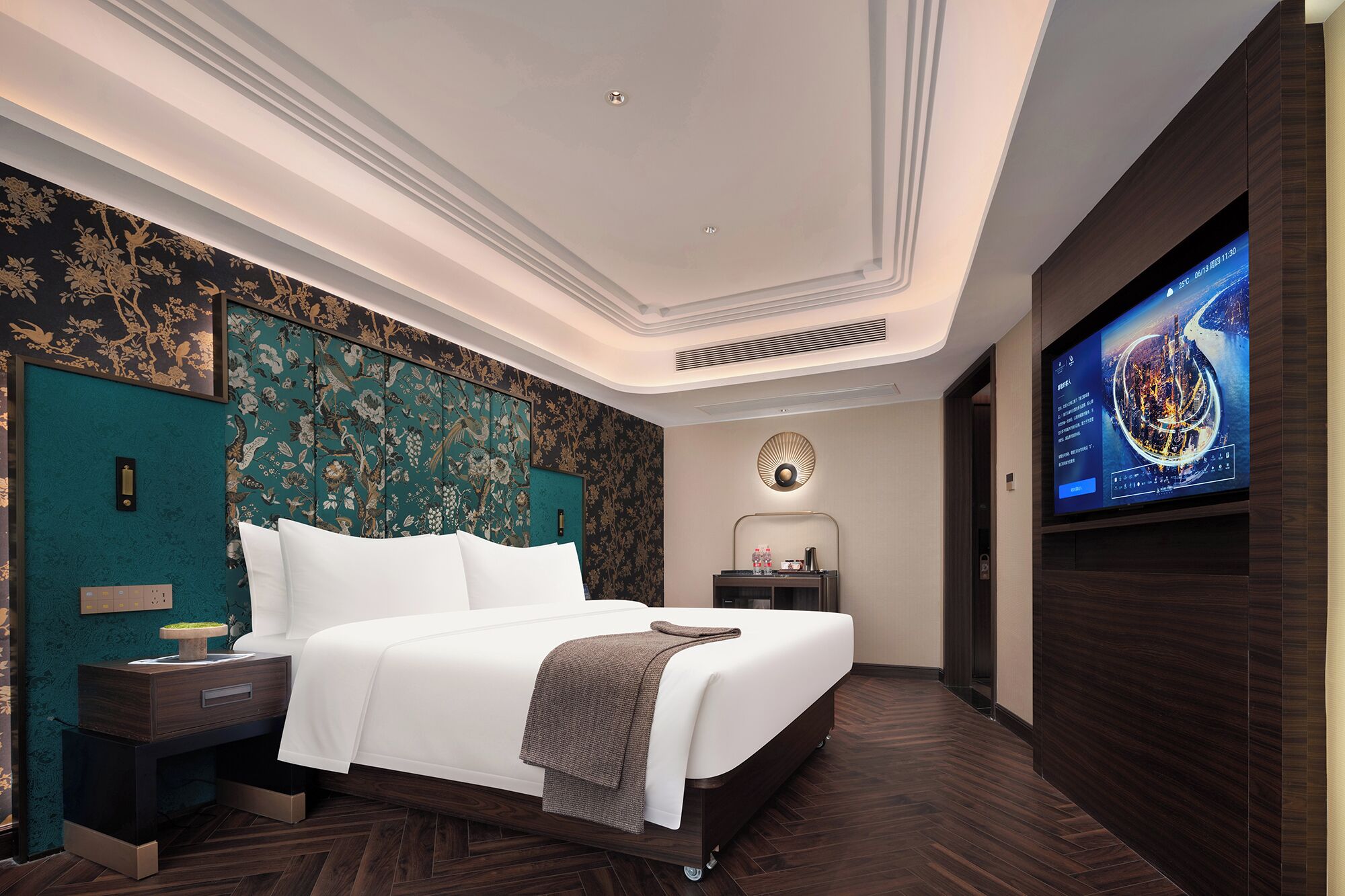 A modern hotel room with a large bed, a flat-screen TV, a nightstand, and a wall-mounted TV.