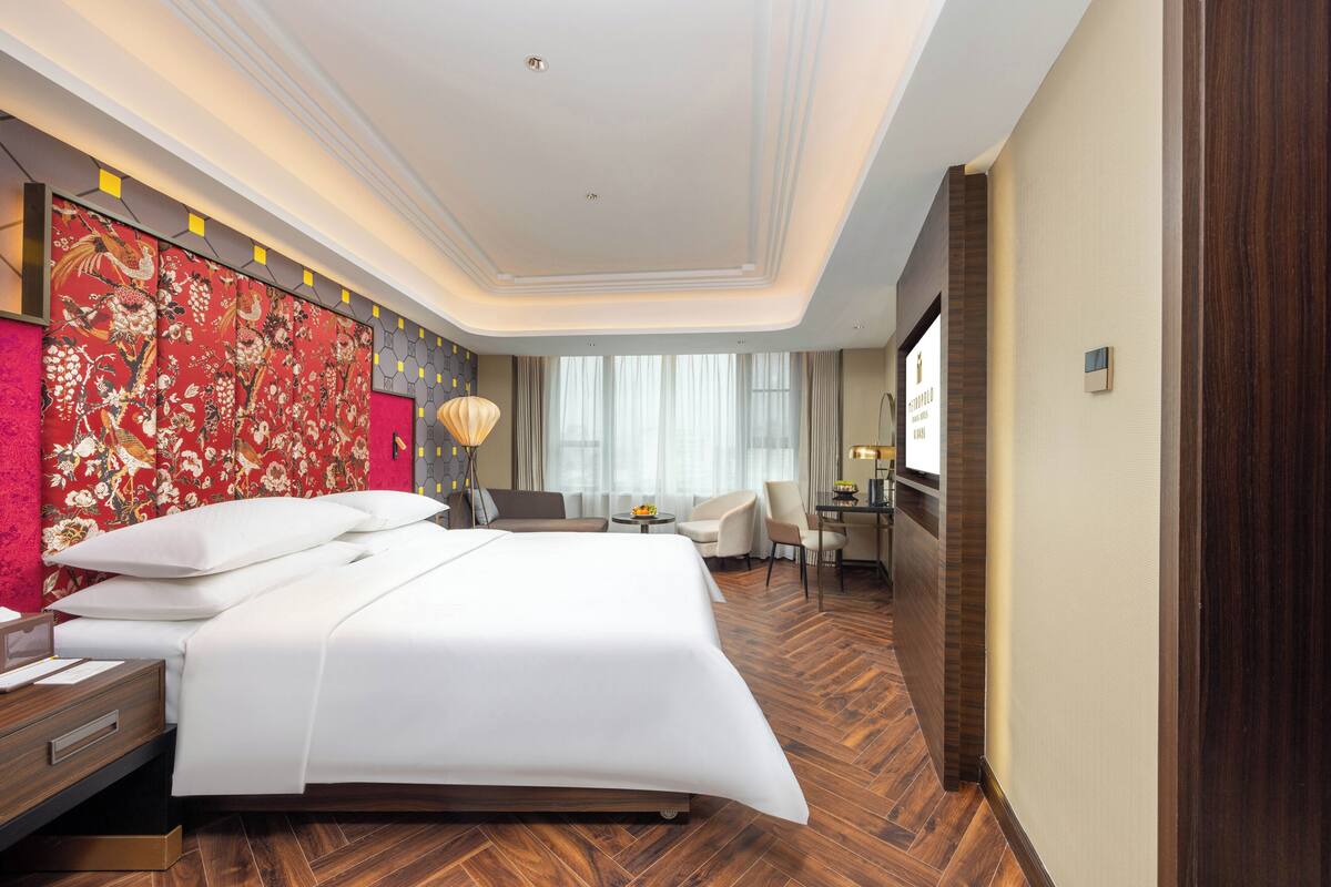 Ein Hotelzimmer mit einem großen Bett, einem Schreibtisch, einem Sessel und einem Fernseher.
