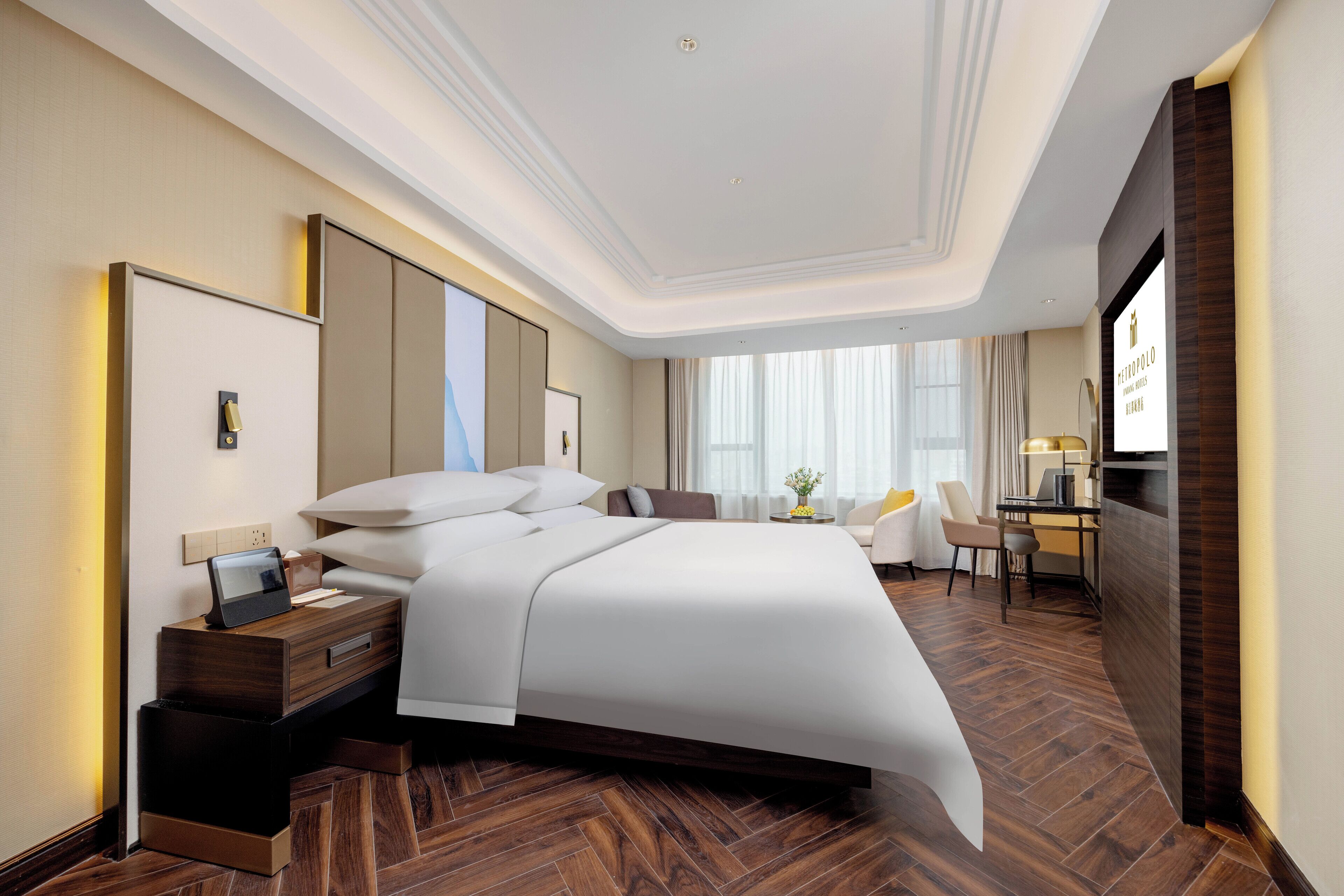 Une chambre d’hôtel moderne avec un grand lit, un bureau avec une chaise, une télévision et une petite table sur laquelle est posé un vase.