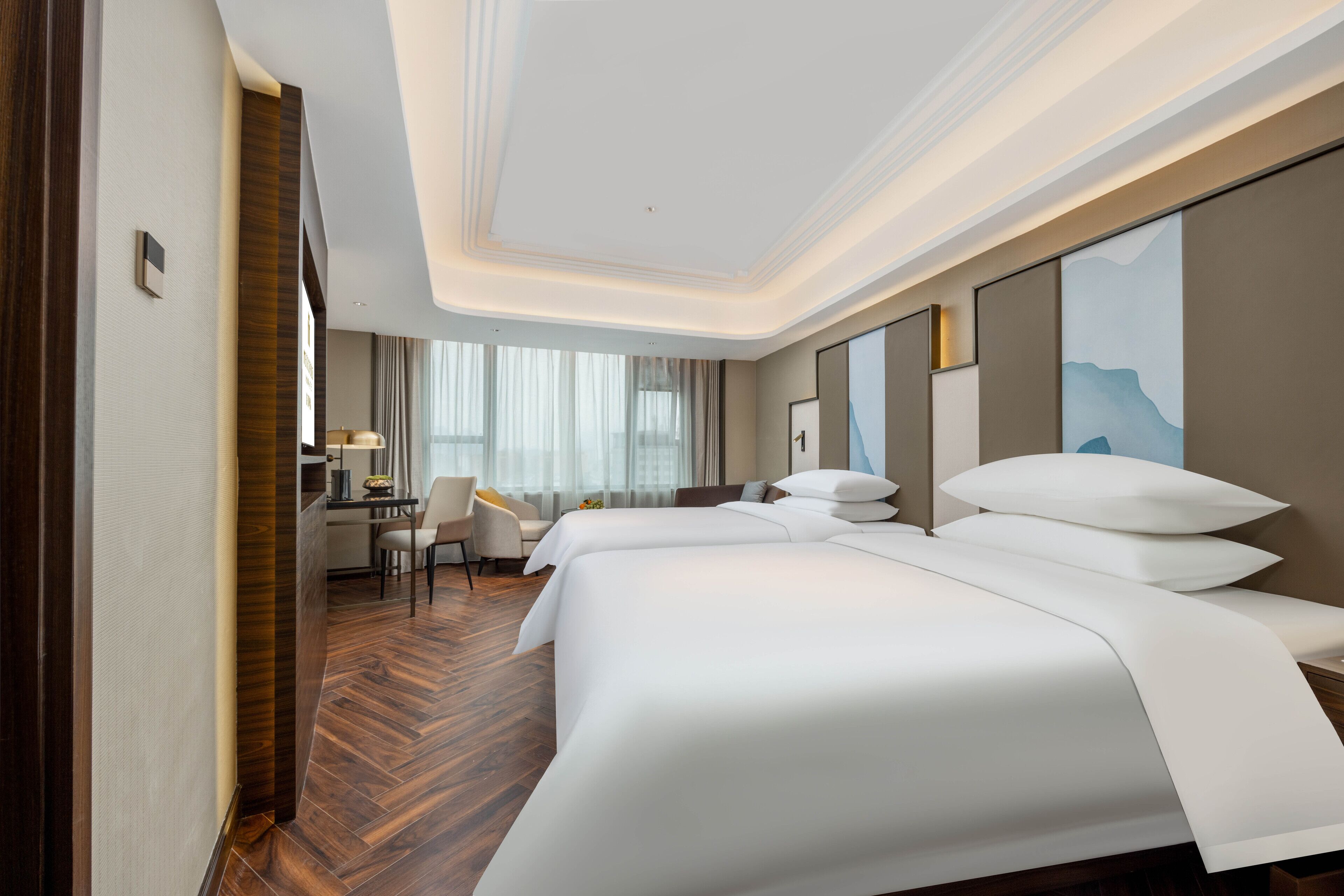 A hotel room with two beds, a desk, a chair, and a large window with curtains.