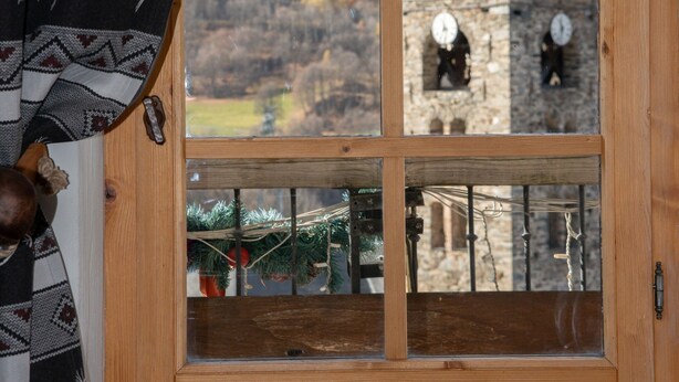 A wooden-framed window with a view of a mountain landscape and a clock tower. - Chalet La Corniche, cozy for 13, sauna with mountain views and private terrace (Les Belleville)