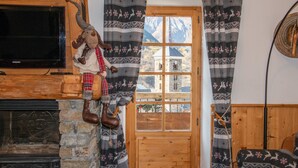 A rustic room with a stone fireplace, a television mounted on the wall, a wooden door with a window, and a patterned curtain. - Chalet La Corniche, cozy for 13, sauna with mountain views and private terrace (Les Belleville)