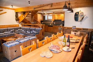 A wooden interior with a dining table set for a meal, a built-in bench seating area, and a kitchen with wooden cabinets. - Chalet La Corniche, cozy for 13, sauna with mountain views and private terrace (Les Belleville)