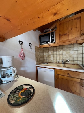 Une cuisine compacte équipée d’une machine à café, d’un four à micro-ondes, d’un évier et de meubles de rangement en bois.