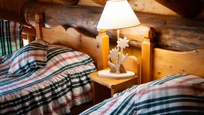 En stuga med träpanel på insidan, inredd med två sängar, ett nattduksbord och en lampa.