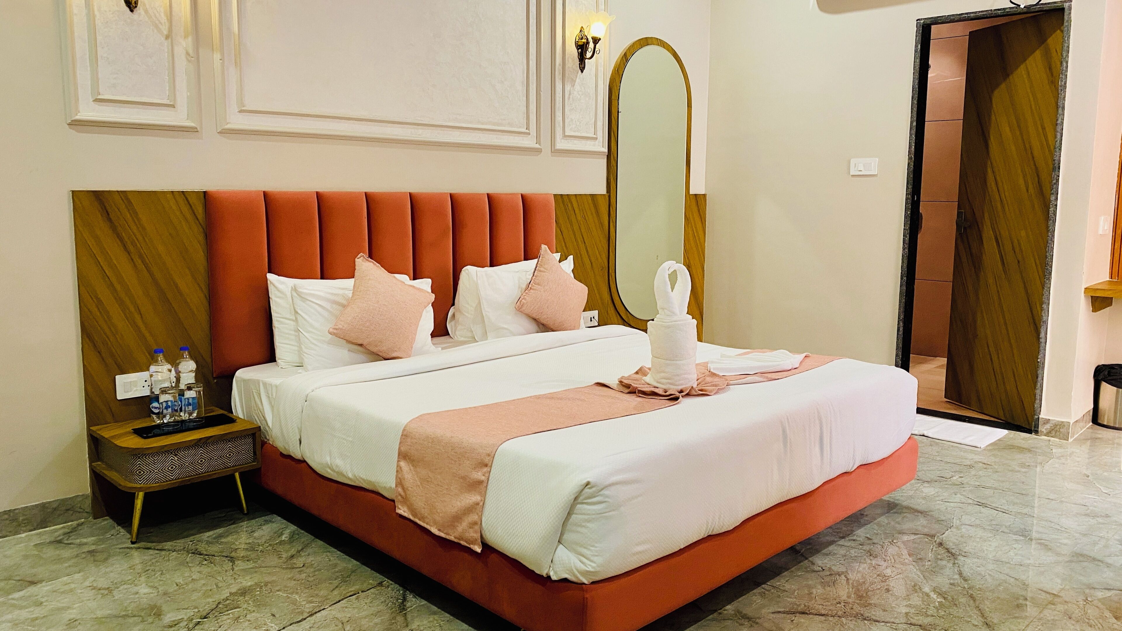 Una habitación de hotel con una cama grande, una mesita de noche, un espejo y una puerta.