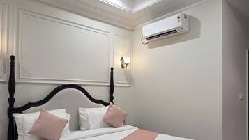 Una cama bien tendida con cabecera, una mesita de noche y un equipo de aire acondicionado instalado en la pared.