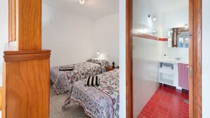 Ein Schlafzimmer mit zwei Betten, einer Holztür, einem Badezimmer mit roten Fliesen und einem Spiegel.