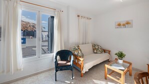 Ein Zimmer mit einer Couch, einem Sessel, einem kleinen Tisch und einem Fenster mit Vorhängen.