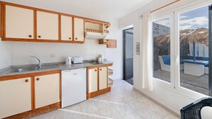 Eine Küche mit Holzausstattung, einem Geschirrspüler, einer Arbeitsplatte mit Wasserkocher und Blick auf einen Pool durch eine Glastür.
