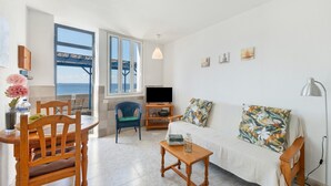A living room with a TV, sofa, wooden table, and chairs. - Apartment 'La Bayana - 2' with Sea View, Shared Pool and Wi-Fi (Los Llanos)
