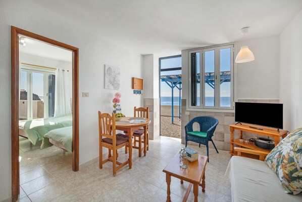 Una habitación con cama, una mesa de comedor con sillas, un mueble para televisión y vista al mar.