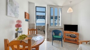A room with a dining table, chairs, a television, and a view of the sea through a window. - Apartment 'La Bayana - 2' with Sea View, Shared Pool and Wi-Fi (Los Llanos)
