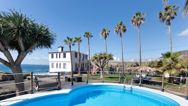 A swimming pool with a view of the ocean, surrounded by palm trees and a white building. - Apartment 'La Bayana - 2' with Sea View, Shared Pool and Wi-Fi (Los Llanos)
