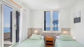 A bedroom with two beds, a window with a view of the sea, a small wooden nightstand, and a wall-mounted picture. - Apartment 'La Bayana - 2' with Sea View, Shared Pool and Wi-Fi (Los Llanos)