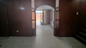 Un corridoio con porte in legno e pavimento in cemento, che conduce a un'area esterna.