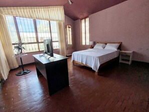 Una habitación con una cama, un escritorio con computadora y una ventana con cortinas.