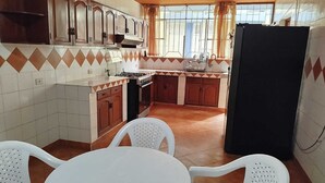 Una cucina con fornello, forno e pensili, un tavolo da pranzo con sedie e un frigorifero.