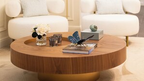A round wooden coffee table with a gold base, a white sofa with a checkered pillow, and a floor lamp with a round light. - Stella Braga Aparthotel (Braga)