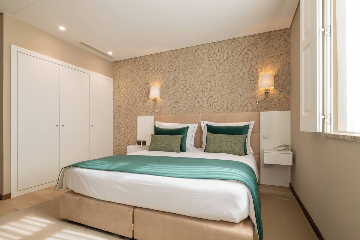 Un dormitorio con una cama grande, dos mesitas de noche, un armario y una lámpara de pared.