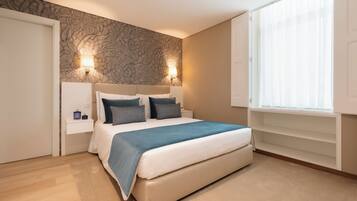 A bedroom with a bed, two bedside lamps, a window with blinds, and a patterned wall.