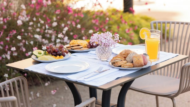 A table set outdoors with plates of food, a glass of orange juice, and a vase of flowers. - Stella Braga Aparthotel (Braga)