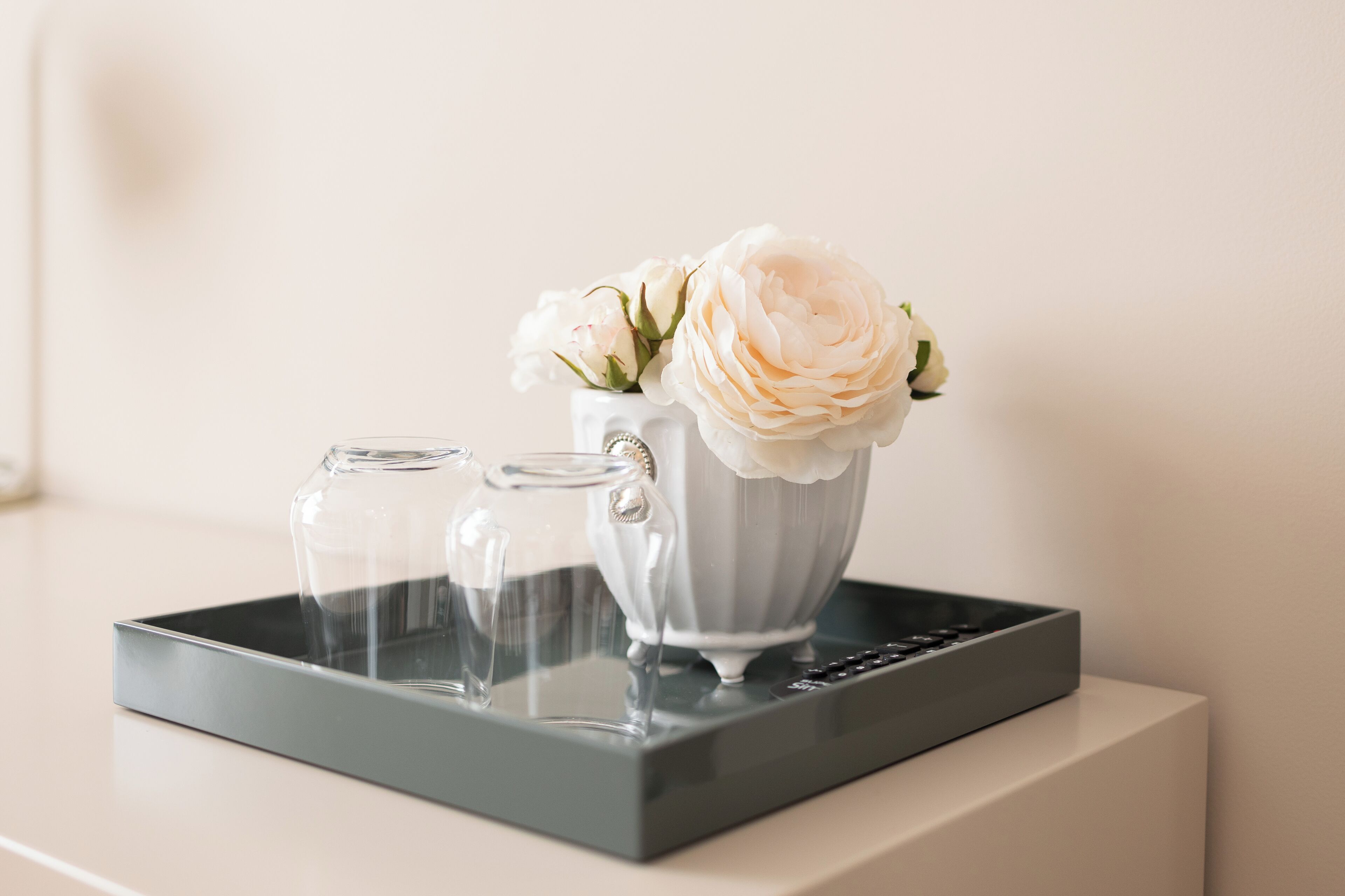 Una bandeja con dos vasos transparentes y un jarrón blanco con flores sobre una superficie blanca.