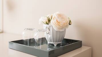 Un plateau avec deux verres transparents et un vase blanc orné de fleurs, le tout posé sur une surface blanche.