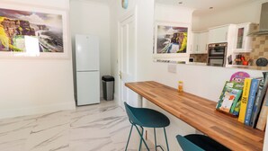 Uma cozinha moderna com bancada de madeira, dois banquetes verde-água, uma geladeira branca e uma lixeira.