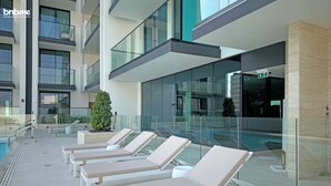 Un moderno vestíbulo de hotel con una zona de piscina acristalada, sillas de descanso y una escalera que conduce a los pisos superiores.