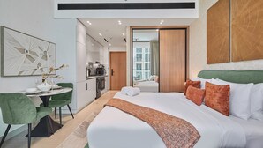 Habitación de hotel moderna con una cama grande, sillas tapizadas en verde, un área de comedor y vistas de la ciudad a través de una puerta corredera.