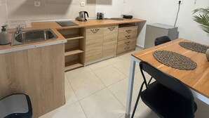 A compact kitchen with a sink, wooden cabinets, a stove, and a dining area with a table and chairs. - Occasus Comfort Room (Halki)