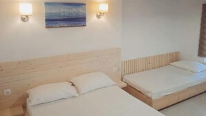 A room with two wooden beds, each with white bedding and a headboard. There are wall-mounted lights and a painting of a seascape. - Occasus Comfort Room (Halki)