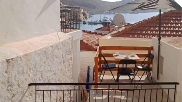 A balcony with a view of a marina, a white wall with an air conditioning unit, and a table with chairs. - Occasus Comfort Room (Halki)