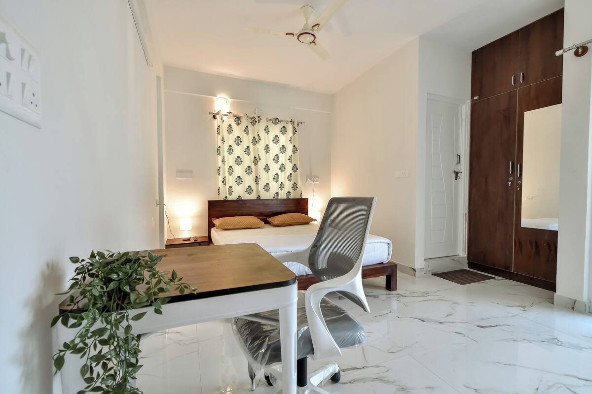 A modern bedroom with a bed, bedside table, and a desk with a chair.