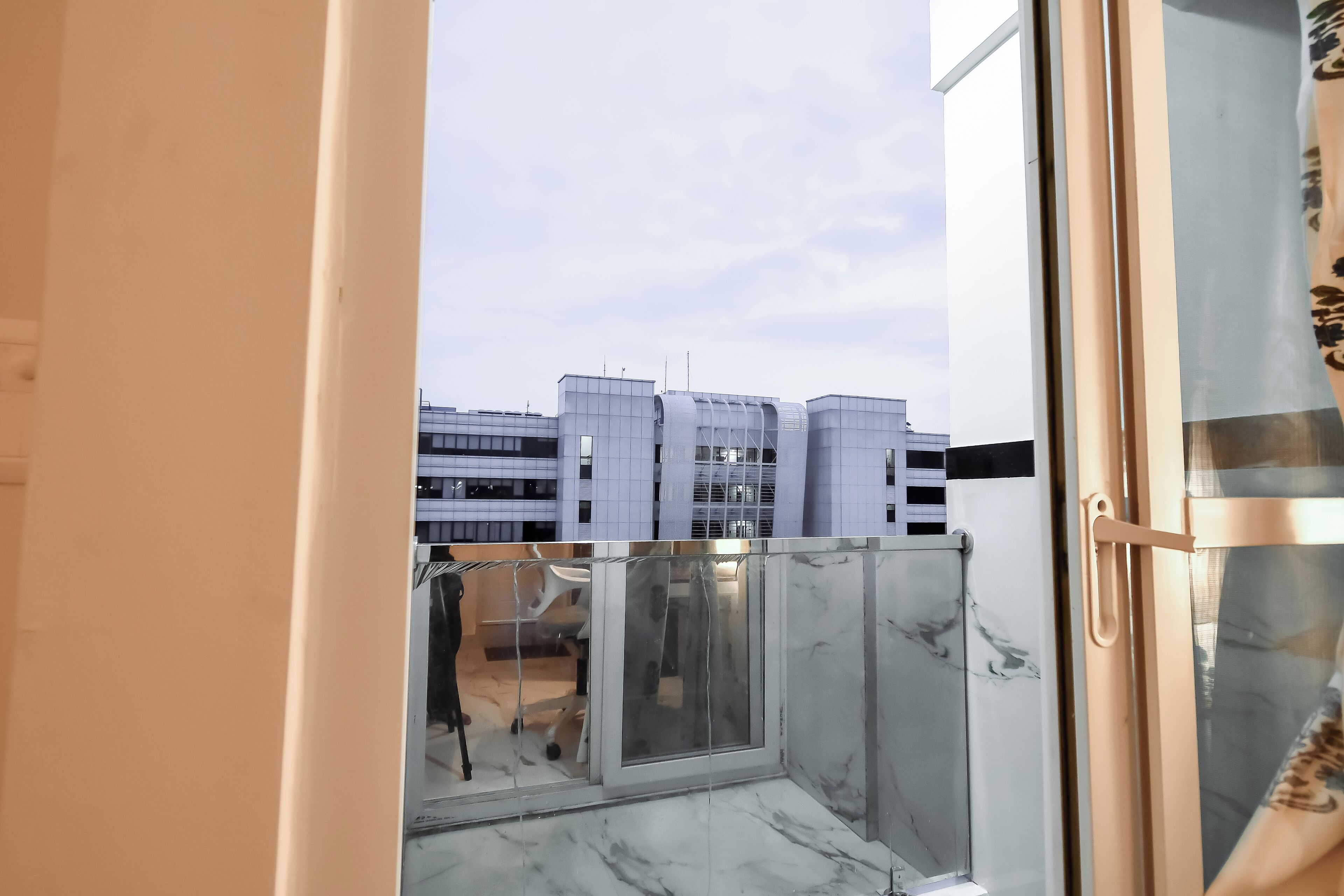 A modern balcony with a glass door, a view of city buildings, and a marble floor.