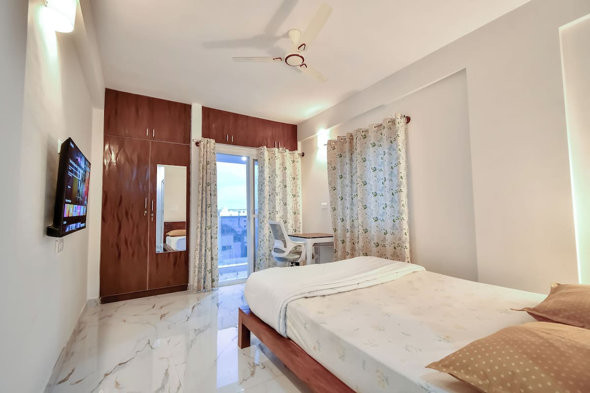 A bedroom with a bed, a desk, a chair, a TV, and a wardrobe.
