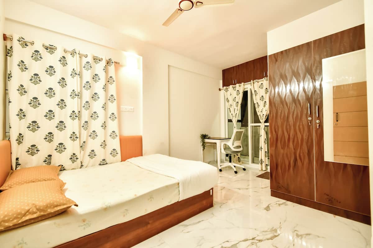 A bedroom with a bed, curtains, a desk, and a wardrobe.