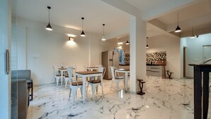 A spacious dining area with a marble floor, white chairs, and pendant lighting. - Namma HomeSlice (Bengaluru)