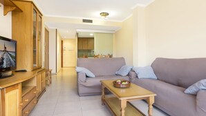 Ένα μοντέρνο σαλόνι με έναν καναπέ, ένα τραπεζάκι σαλονιού και μια τηλεόραση τοποθετημένη πάνω σε ένα ξύλινο έπιπλο.