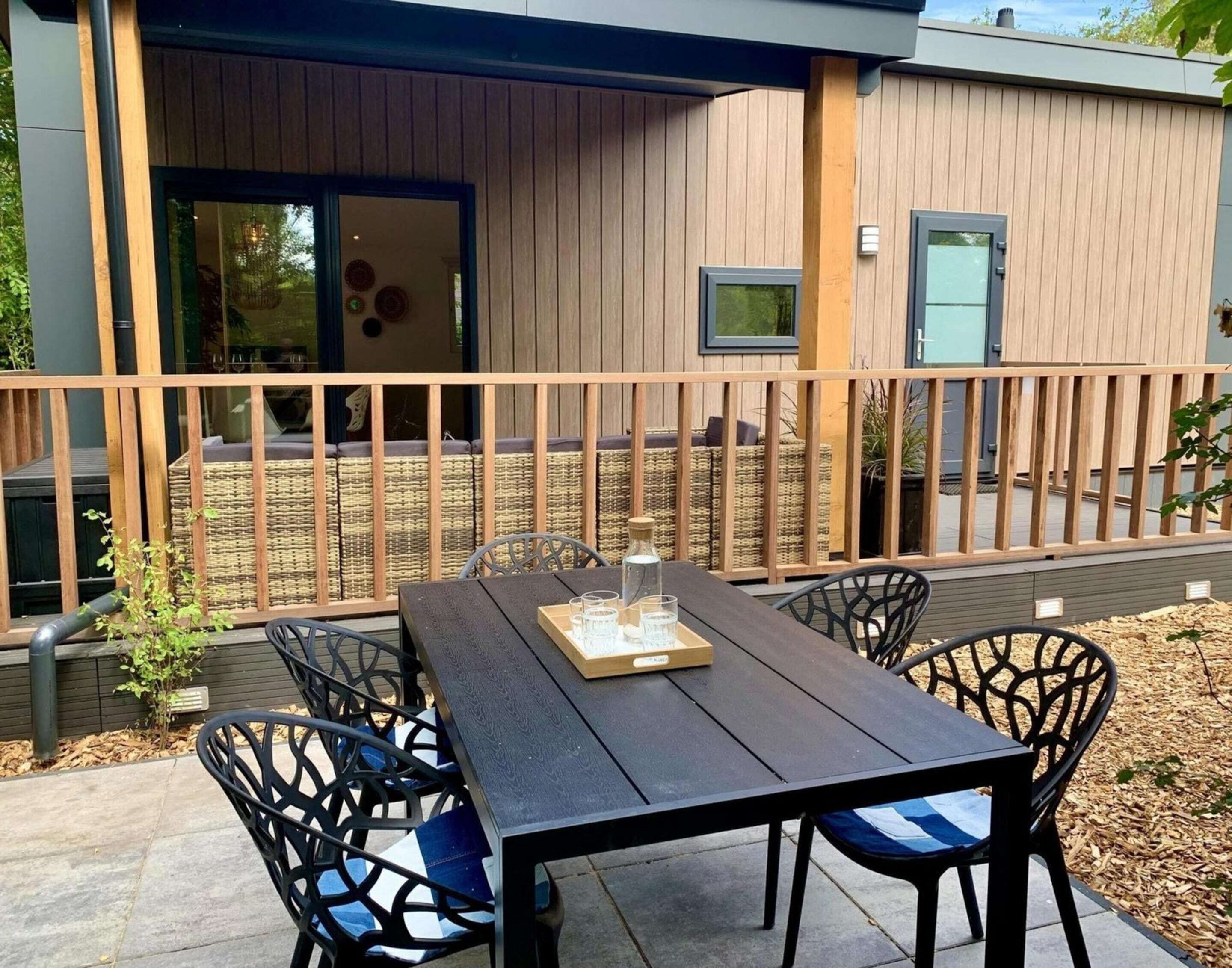 A wooden deck with a table and chairs, a small outdoor seating area with cushions, and a door leading to the interior.