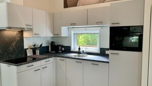 Une cuisine moderne avec des meubles blancs, un plan de travail noir et une fenêtre donnant sur un espace verdoyant.