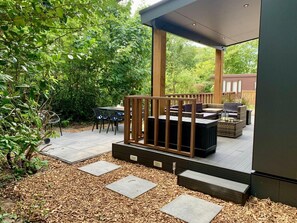 A covered outdoor patio with a wooden deck, seating area, and a table with chairs. - Modern Chalet With Terrace, Veranda (Sint Maartensvlotbrug)