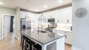 A modern kitchen with white cabinets, a large island with stools, stainless steel appliances, and pendant lighting. - Monty by AvantStay | 4BDR 4BA | Balcony + Outdoor Seating | Minutes to Downtown (Nashville)